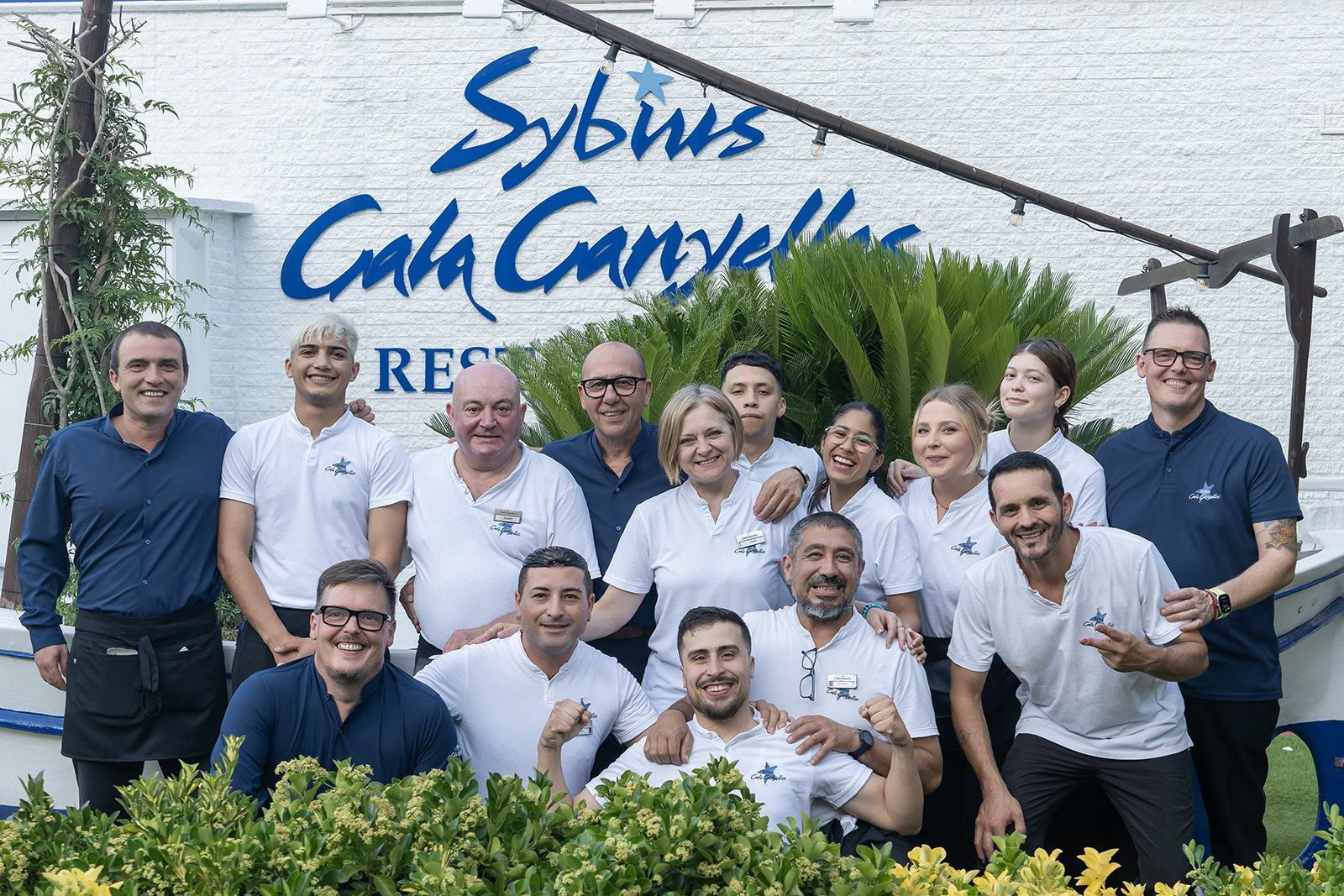 Equipo del restaurante Sybius en Cala Canyelles, Lloret de Mar, reunido frente a la fachada del restaurante especializado en cocina mediterránea, mariscos, arroces y carnes a la brasa. Equip del restaurant Sybius a Cala Canyelles, Lloret de Mar, reunit davant de la façana del restaurant especialitzat en cuina mediterrània, marisc, arrossos i carns a la brasa. Team of Sybius restaurant in Cala Canyelles, Lloret de Mar, gathered in front of the restaurant specializing in Mediterranean cuisine, seafood, rice dishes and grilled meats. Équipe du restaurant Sybius à Cala Canyelles, Lloret de Mar, réunie devant la façade du restaurant spécialisé dans la cuisine méditerranéenne, les fruits de mer, les plats de riz et les viandes grillées.